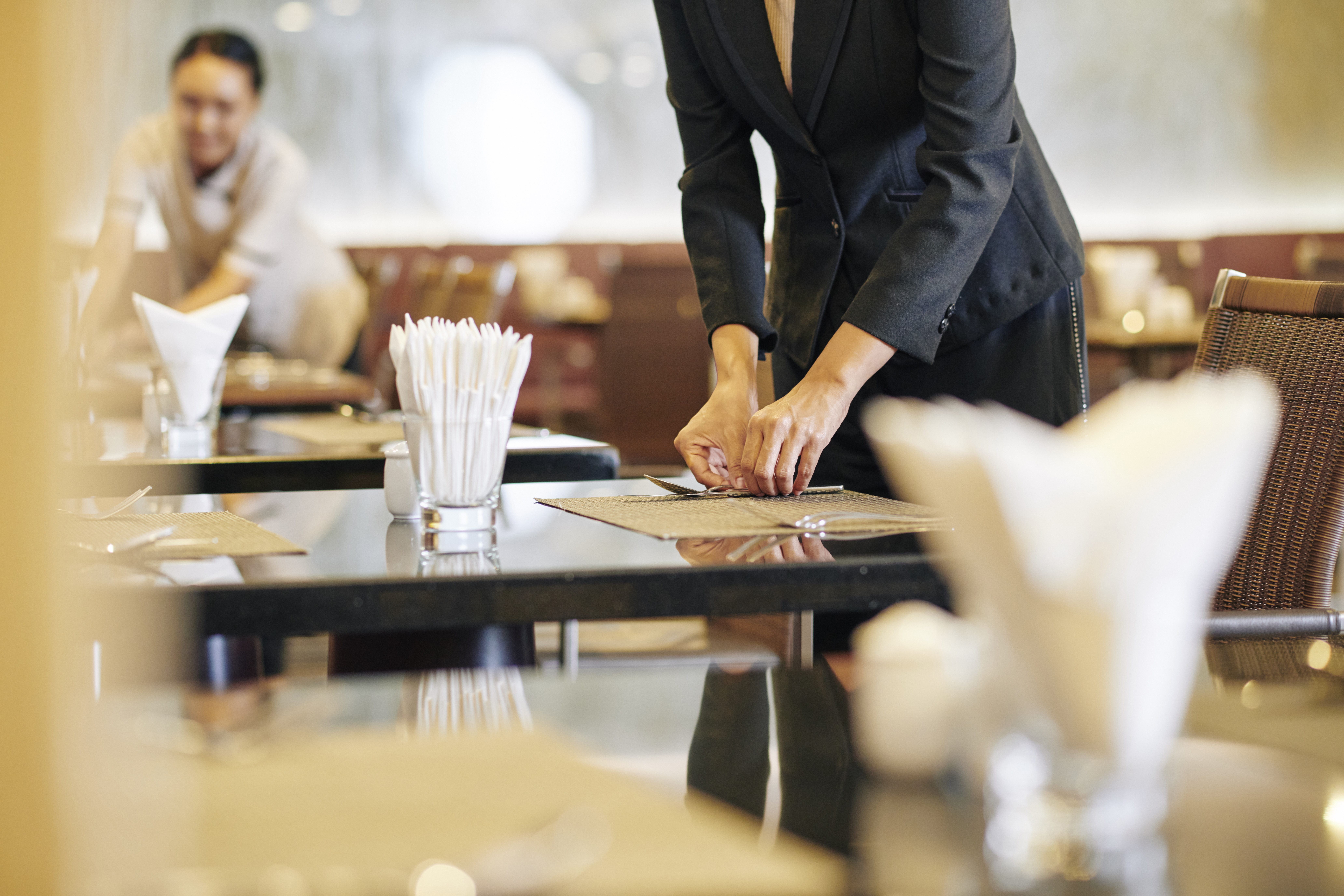 Close-up of manager laying the table at the restaurant with waitress working in the background